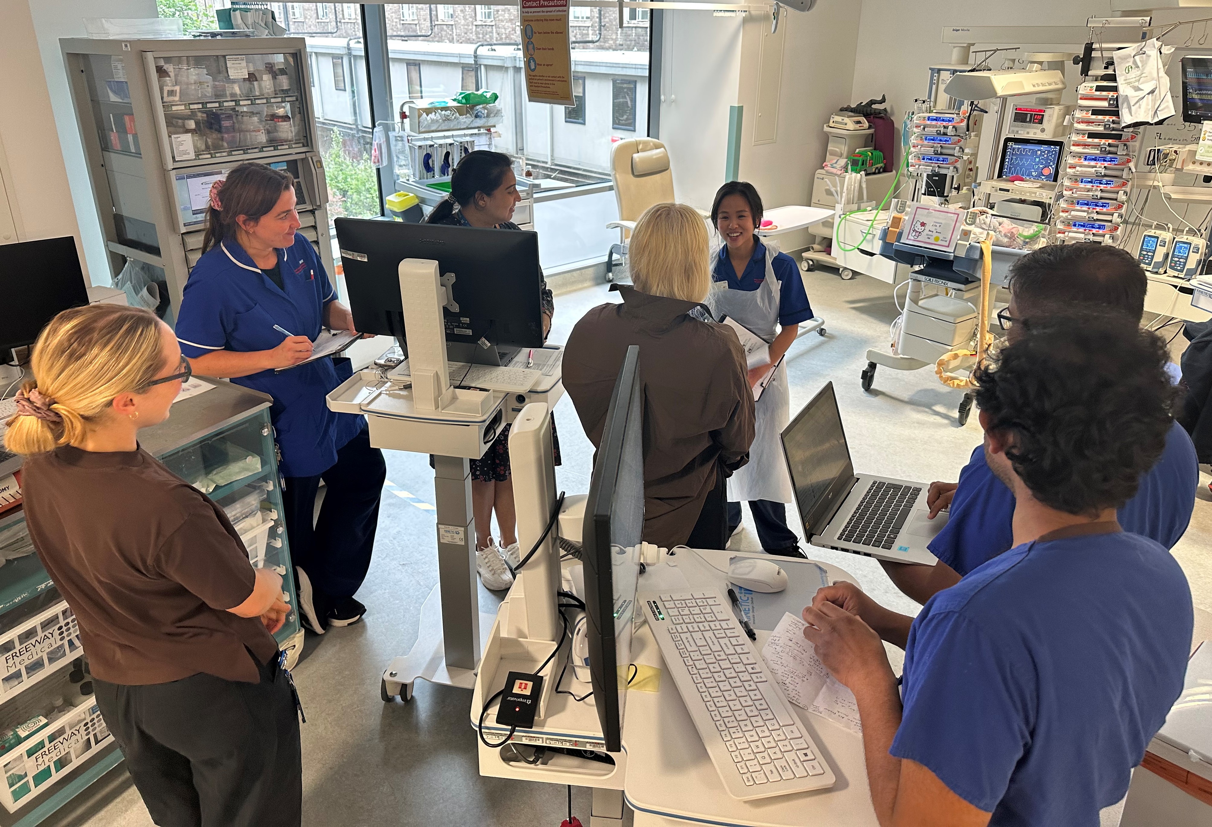 مجموعة من الأطباء والممرضين واقفون حول أجهزة العناية المركزة في وسط غرفة العناية المركزة بينما يتناقشون.