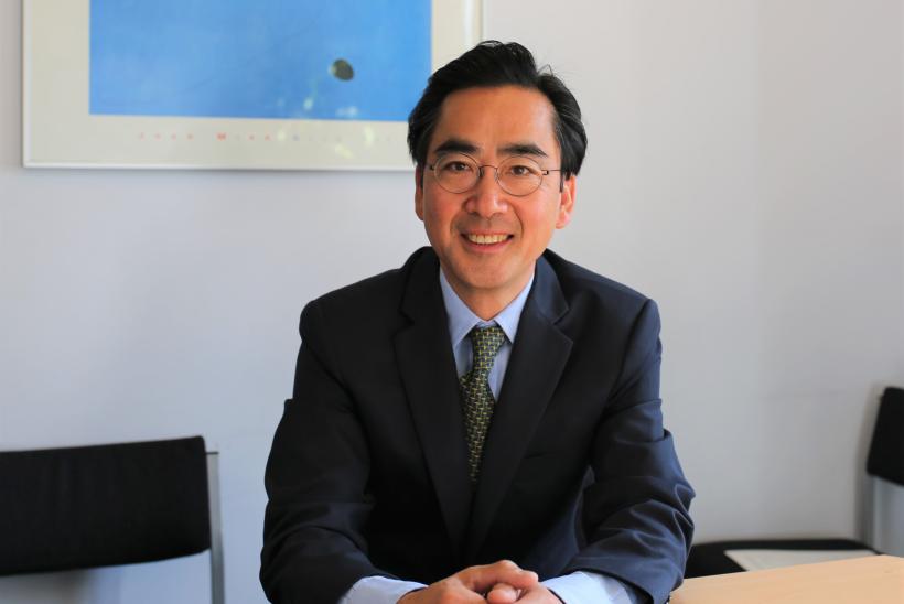 بروفيسور فكتور تسانج جالساً في قاعة إجتماعات على طاولة ووراؤه لوحة فنية