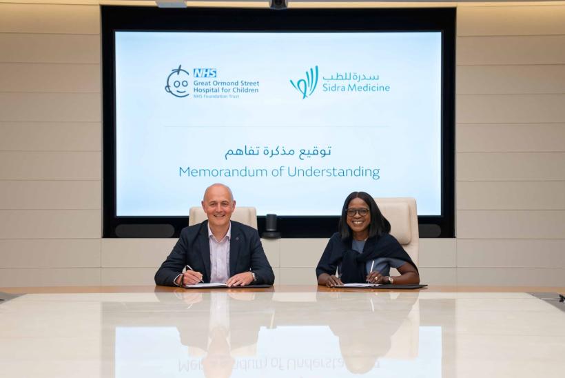 GOSH CEO Matt Shaw and CEO of SIDRA Hospital Group Qatar sitting in a room with a huge screen behind them showing the event name signing the MoUU