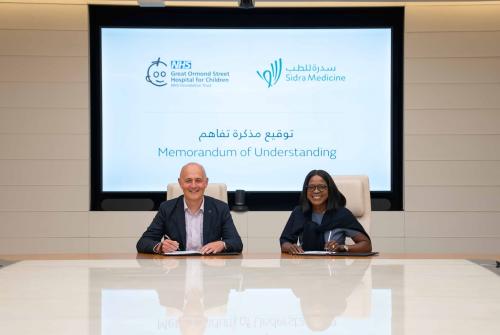 GOSH CEO Matt Shaw and CEO of SIDRA Hospital Group Qatar sitting in a room with a huge screen behind them showing the event name signing the MoUU