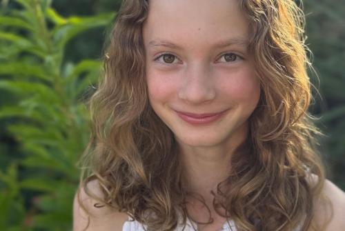 Aurelia standing in front of a tree with the sunlight behind her reflecting on her hair