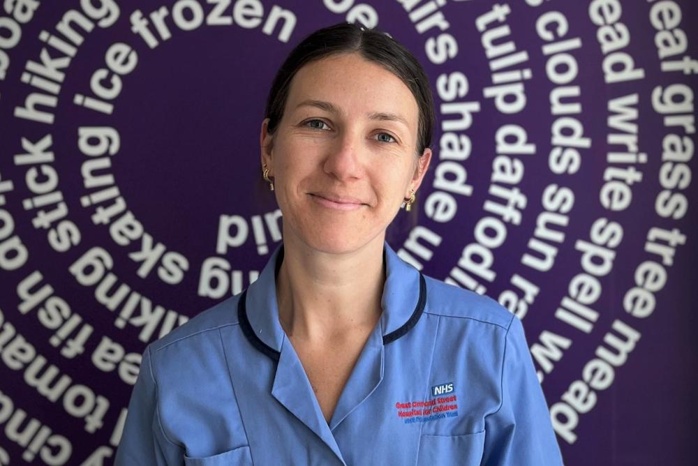 Butterfly Ward: Bonnie Rapson, photographed in front of a mural in GOSH showing English white writing in a cyclical pattern against a blue background