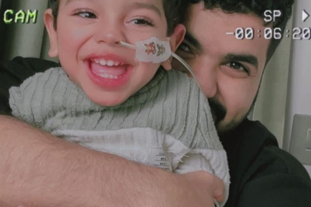 عز يبتسم للكاميرا بينما يحمله والده فهد