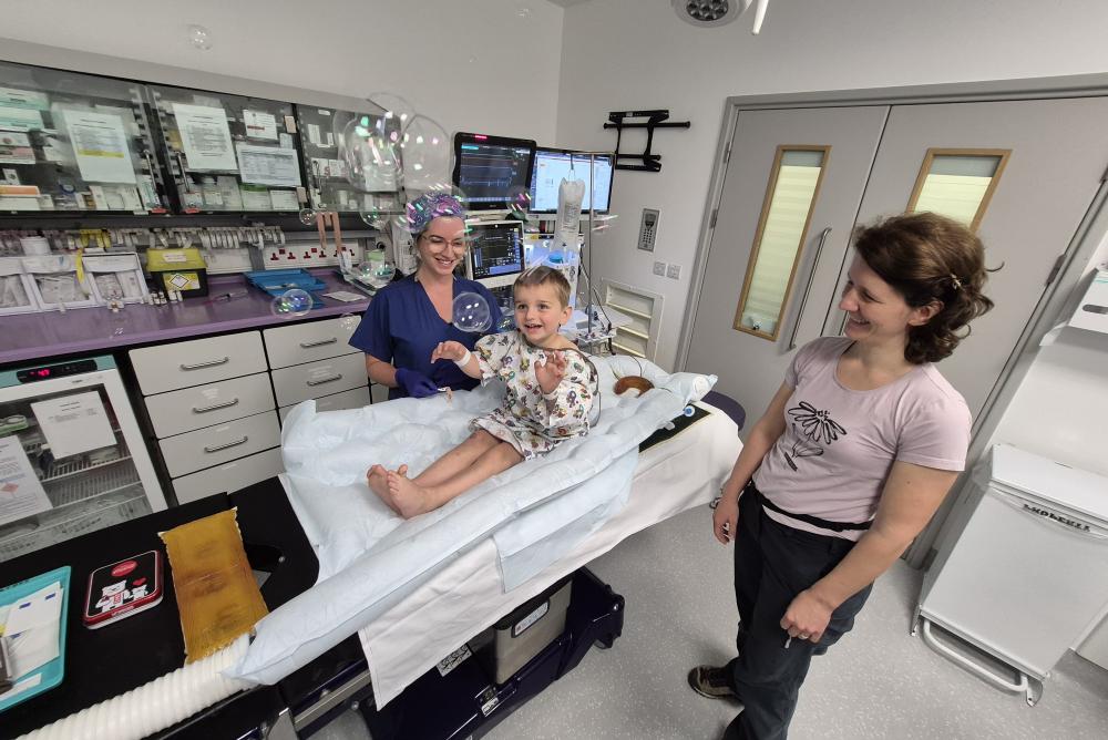 كريستوف في غرفة العمليات قبل إجراء العملية وأحد أفراد الطاقم يلاعبه بالفقاعات لتسليته بينما تكتمل عملية التخدير.